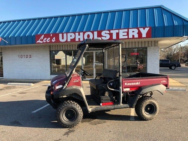 A red kawasaki utility vehicle is parked in front of lee 's upholstery