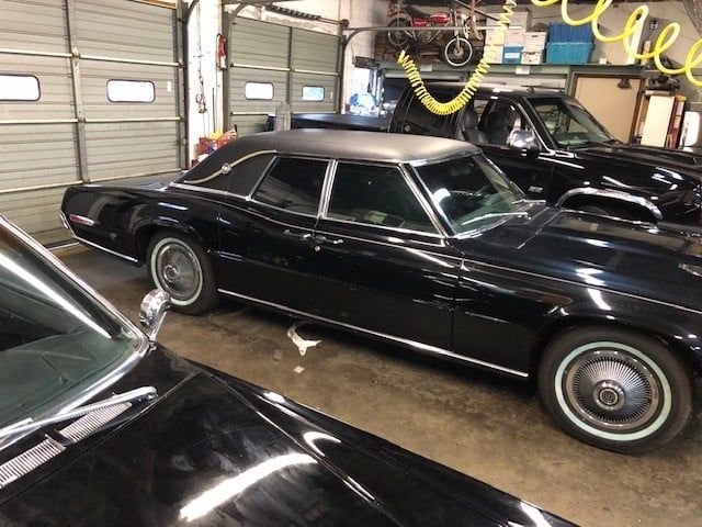 A black car is parked in a garage next to another car.