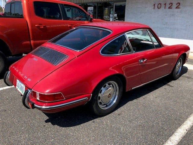 A red porsche is parked in a parking lot next to an orange truck