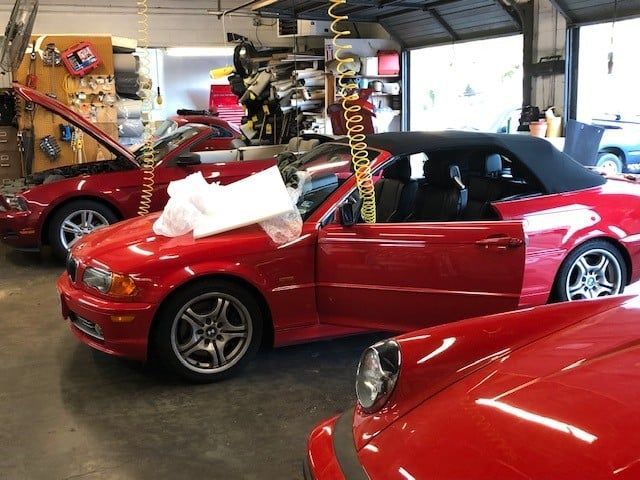 Two red cars are parked in a garage with their hoods open
