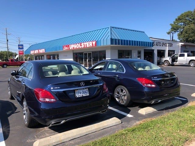Two cars are parked in front of a store called upholstery