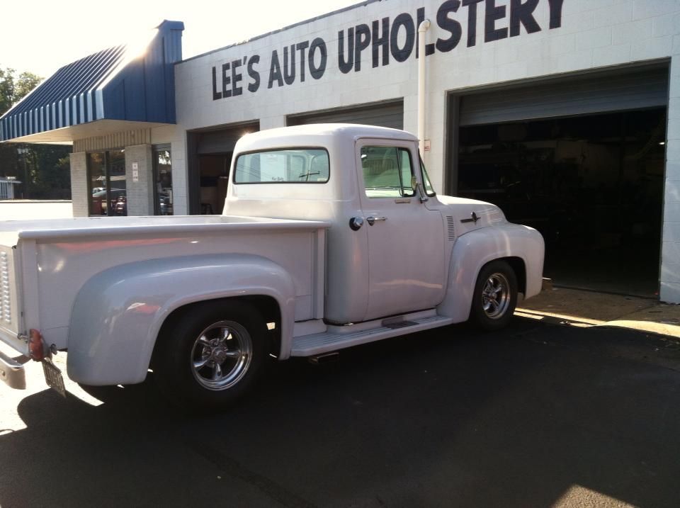 A white truck is parked in front of lee 's auto upholstery