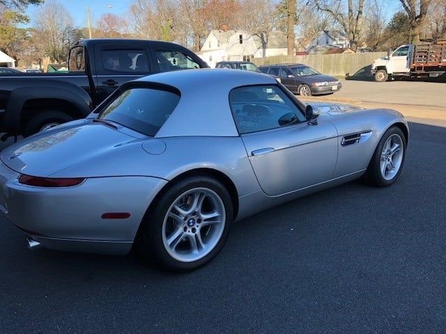 A silver sports car is parked on the side of the road next to a truck.