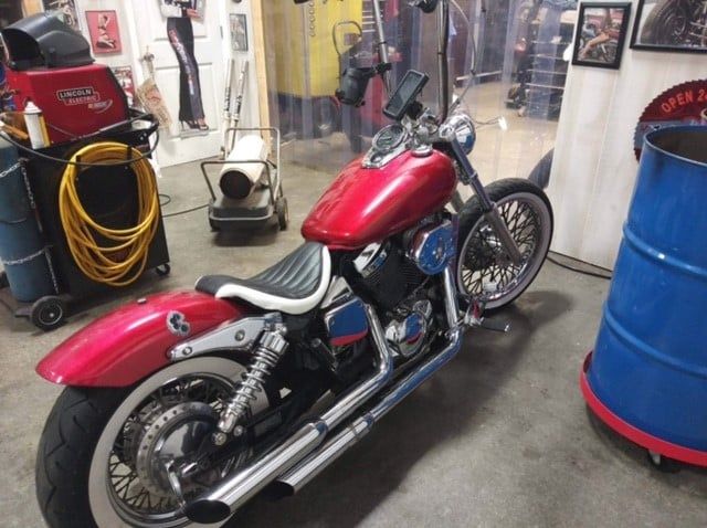 A red motorcycle is parked in a garage next to a blue barrel