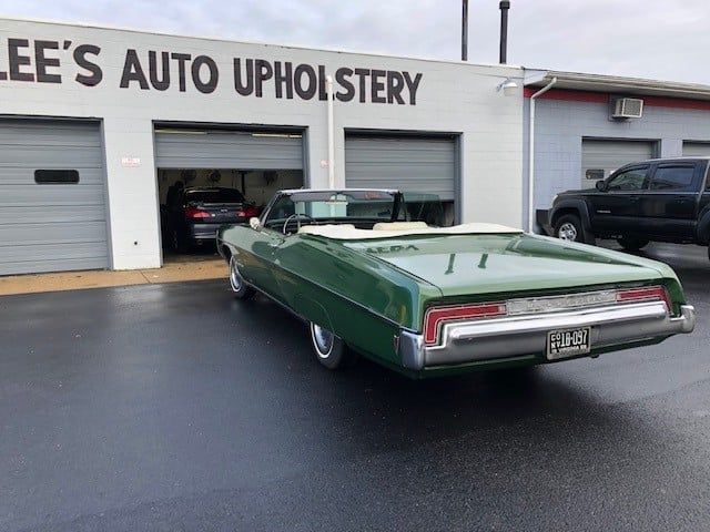 A green car is parked in front of lee 's auto upholstery