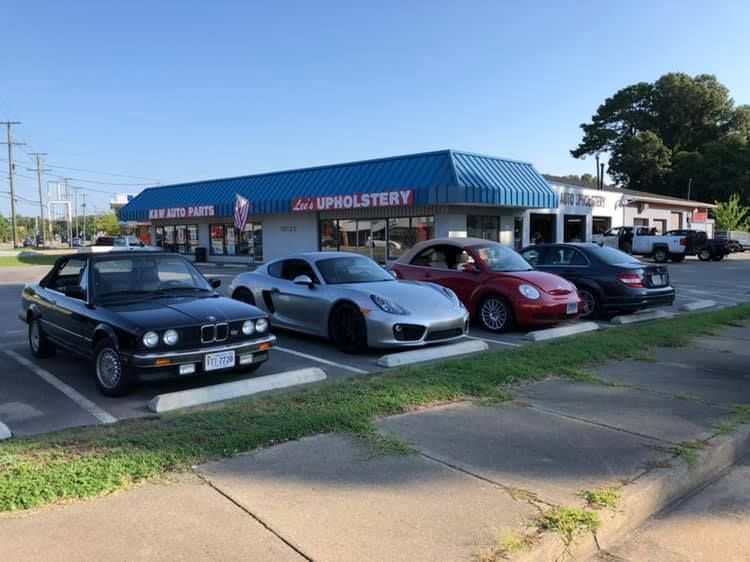 A row of cars are parked in front of a upholstery shop.