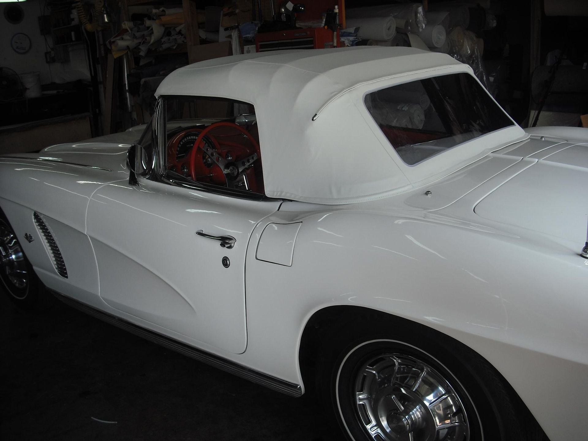 A white car with a red steering wheel is parked in a garage