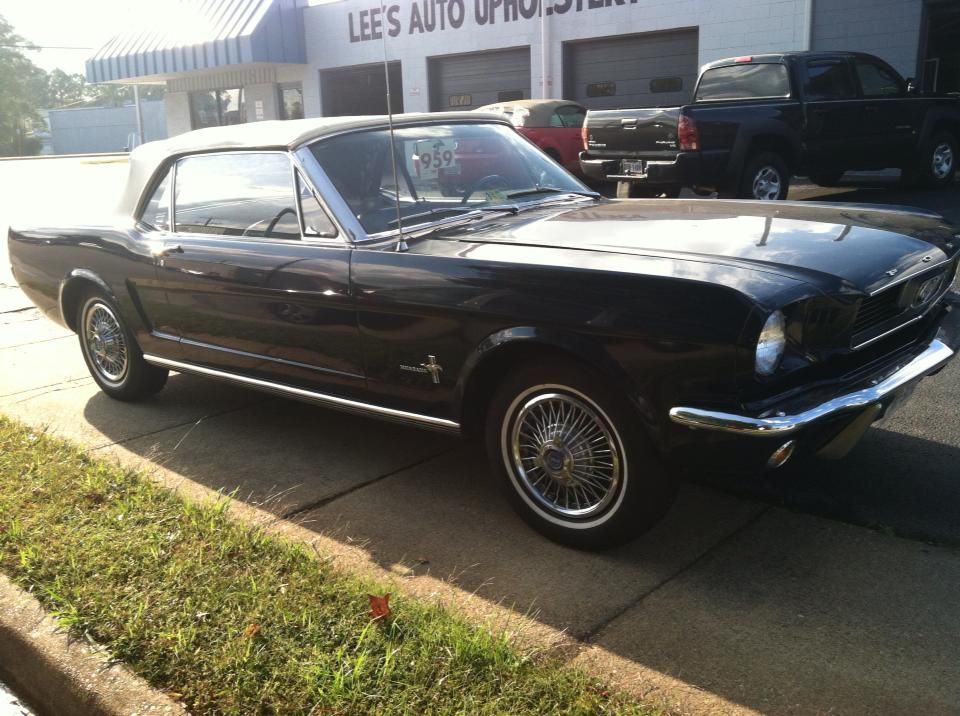 A black mustang is parked in front of a lee 's auto office