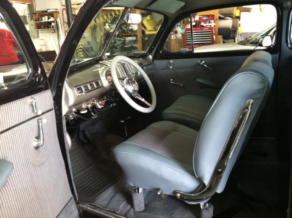 The inside of an old car with blue seats and a steering wheel