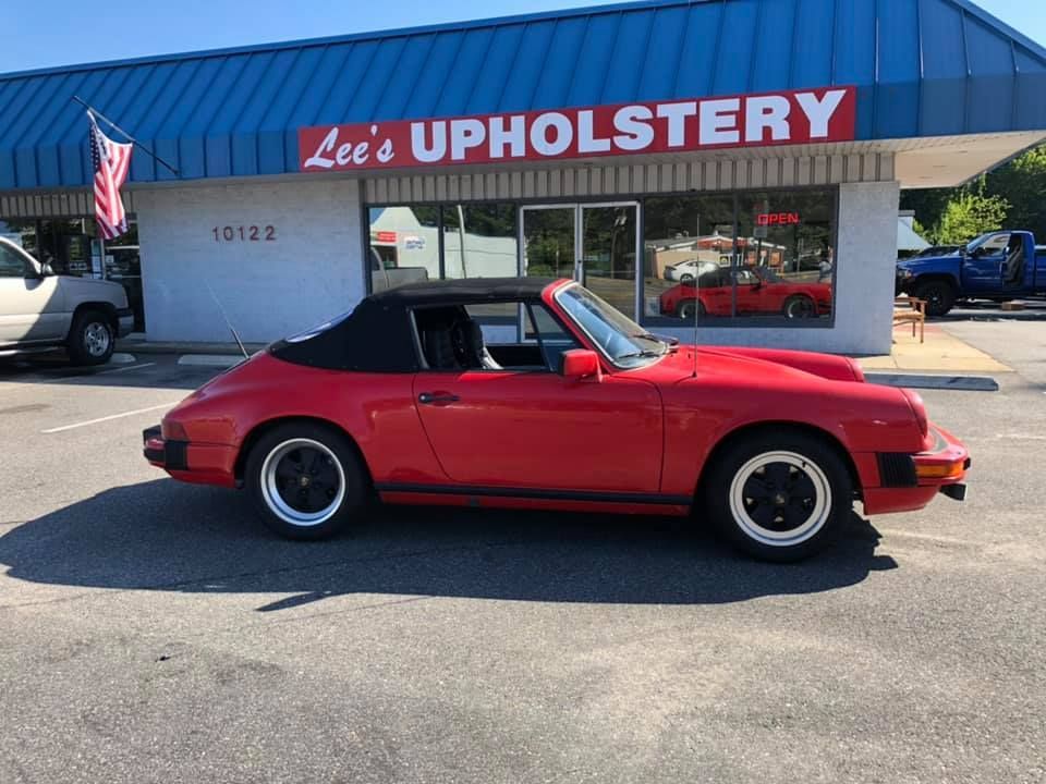 A red car is parked in front of a lee 's upholstery store.