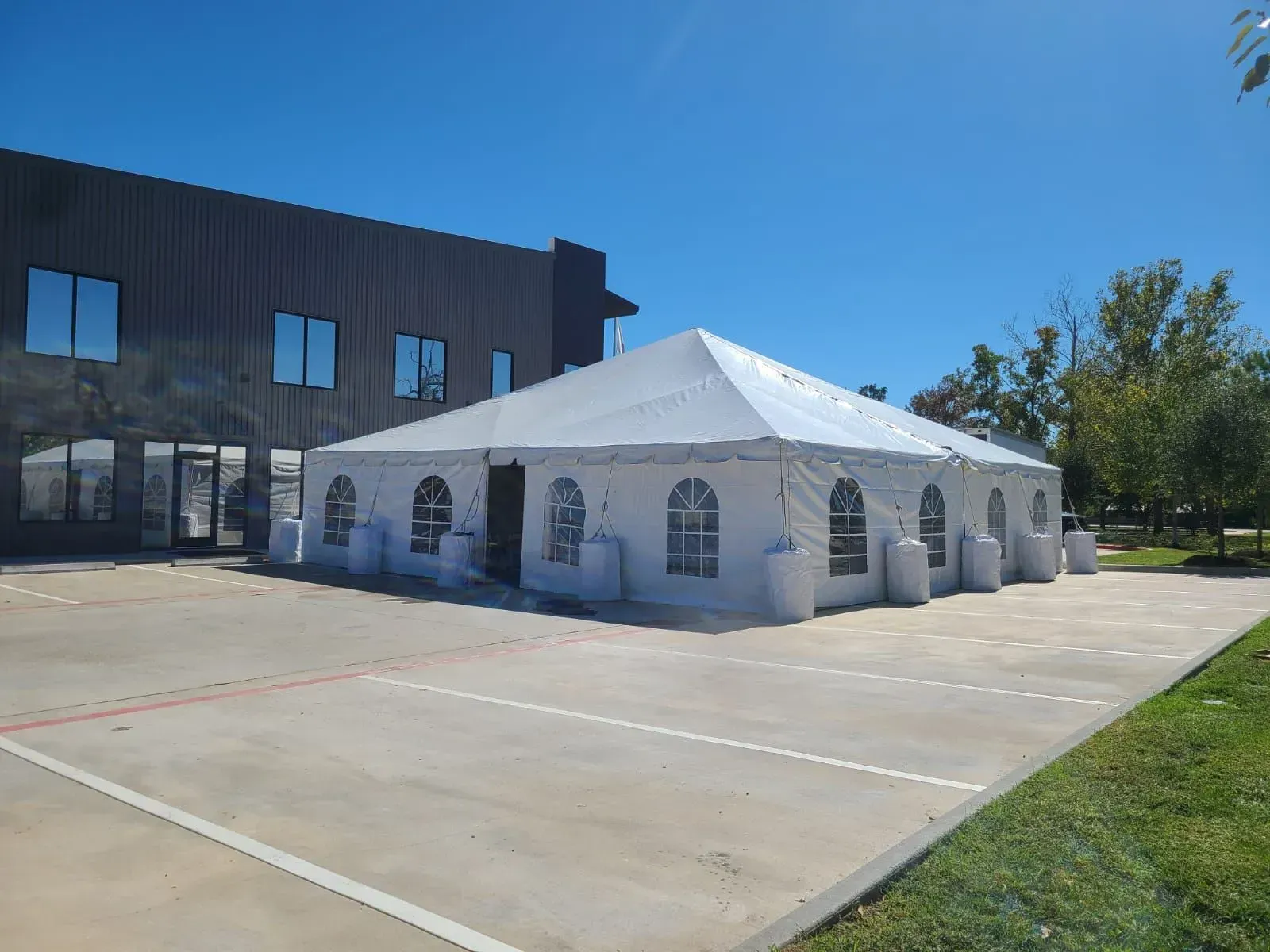 White tent set up in a parking lot, next to a modern building under a bright blue sky.