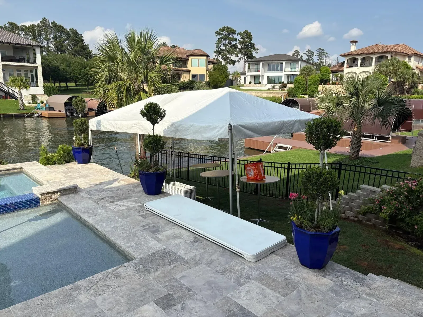 Tent set up near a pool and waterfront, with tables and potted plants.