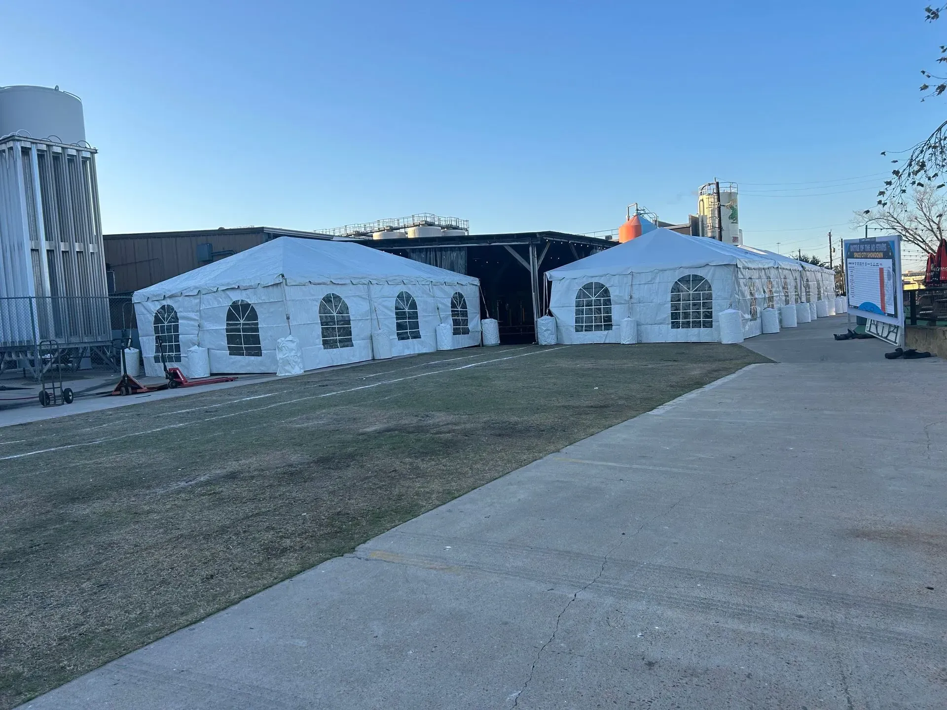 Two white tents on a grassy area next to a paved pathway. A water tower is in the background.