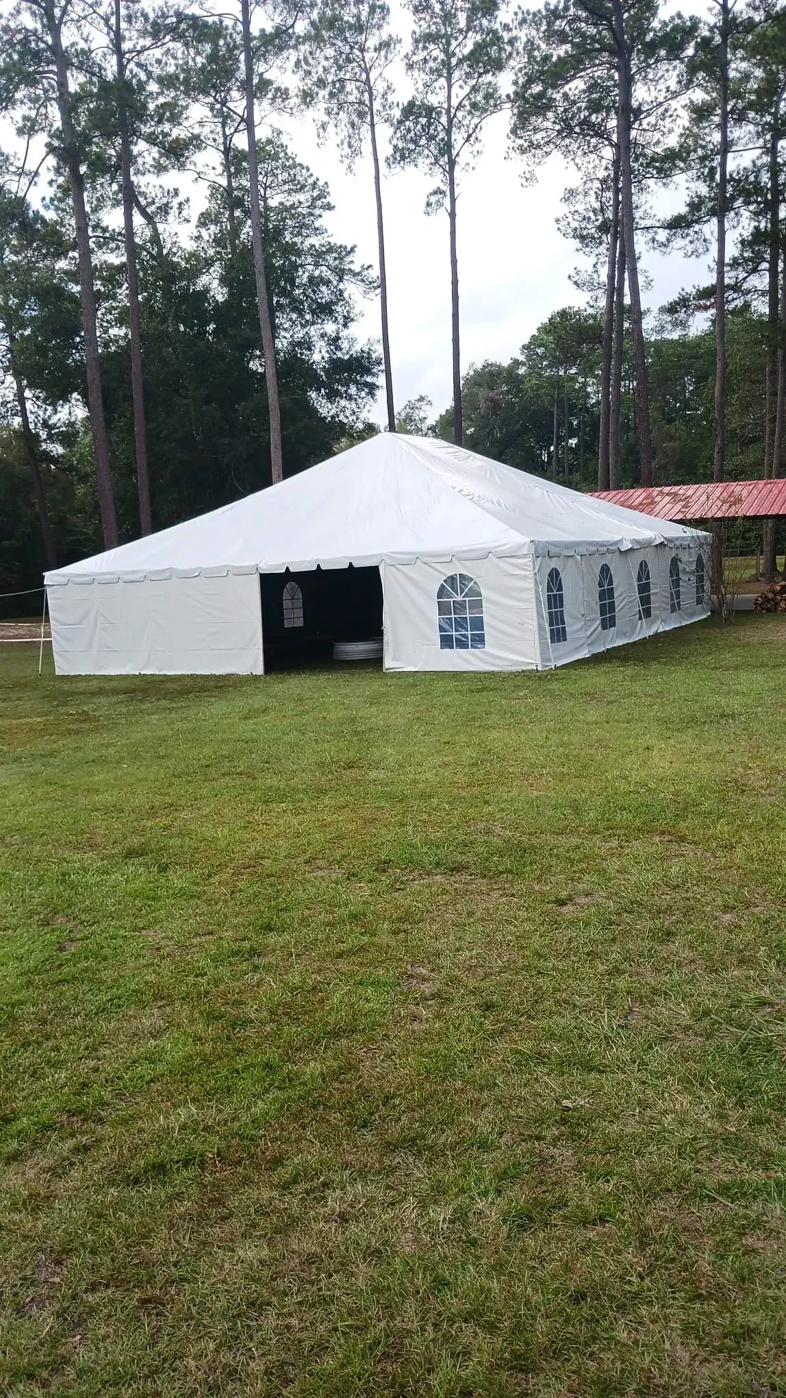 White party tent on green grass with trees in the background.