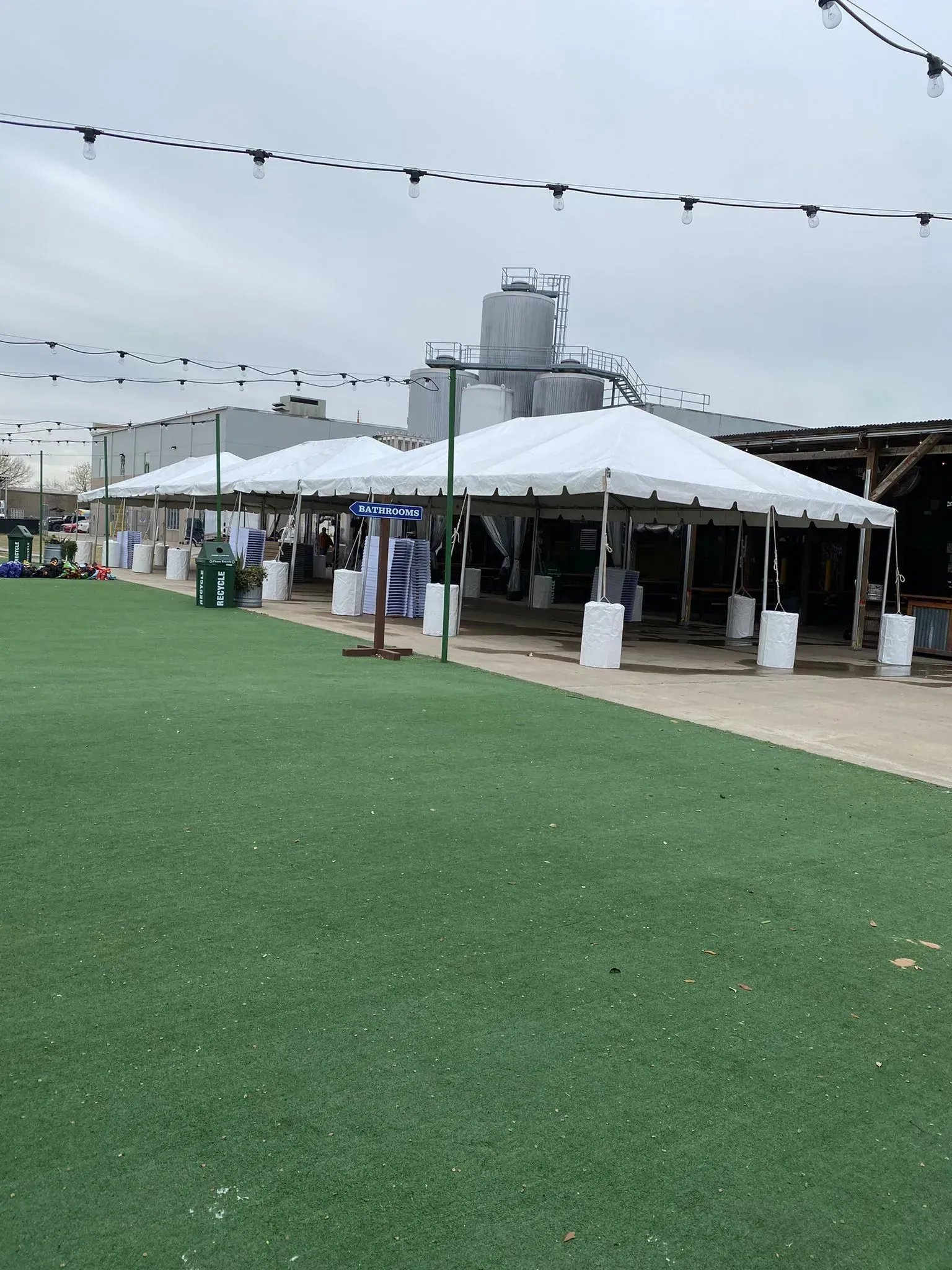 White tents on a green lawn with a paved walkway, possibly an outdoor market under a cloudy sky.