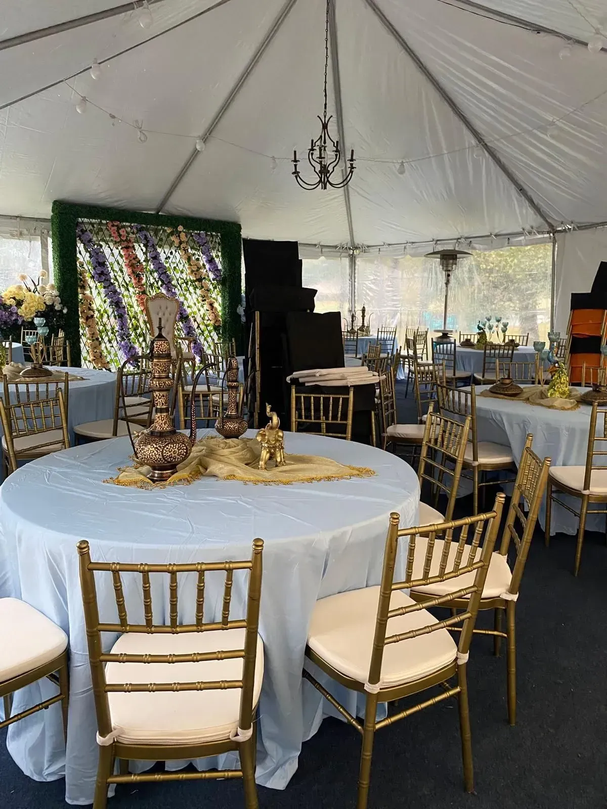 Inside a large tent: tables set with light blue tablecloths and gold chairs, decorative items, and a chandelier.
