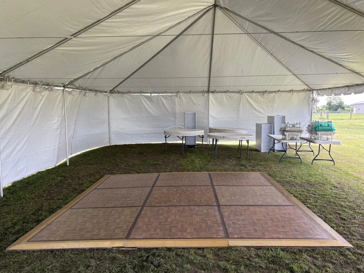 Inside a white tent: dance floor, tables with food, and serving equipment on grass.