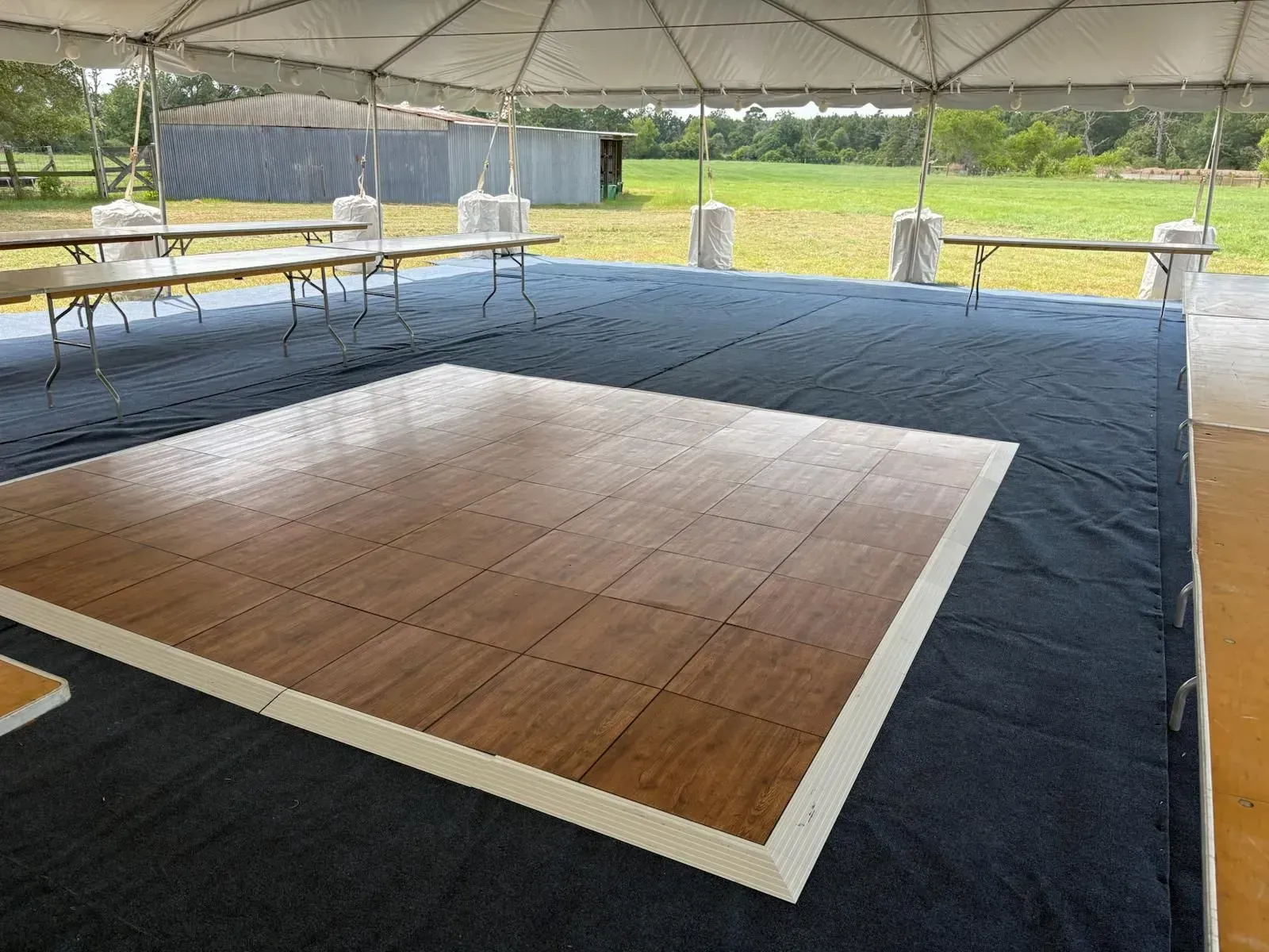Wooden dance floor under a tent with tables, grassy field in the background.