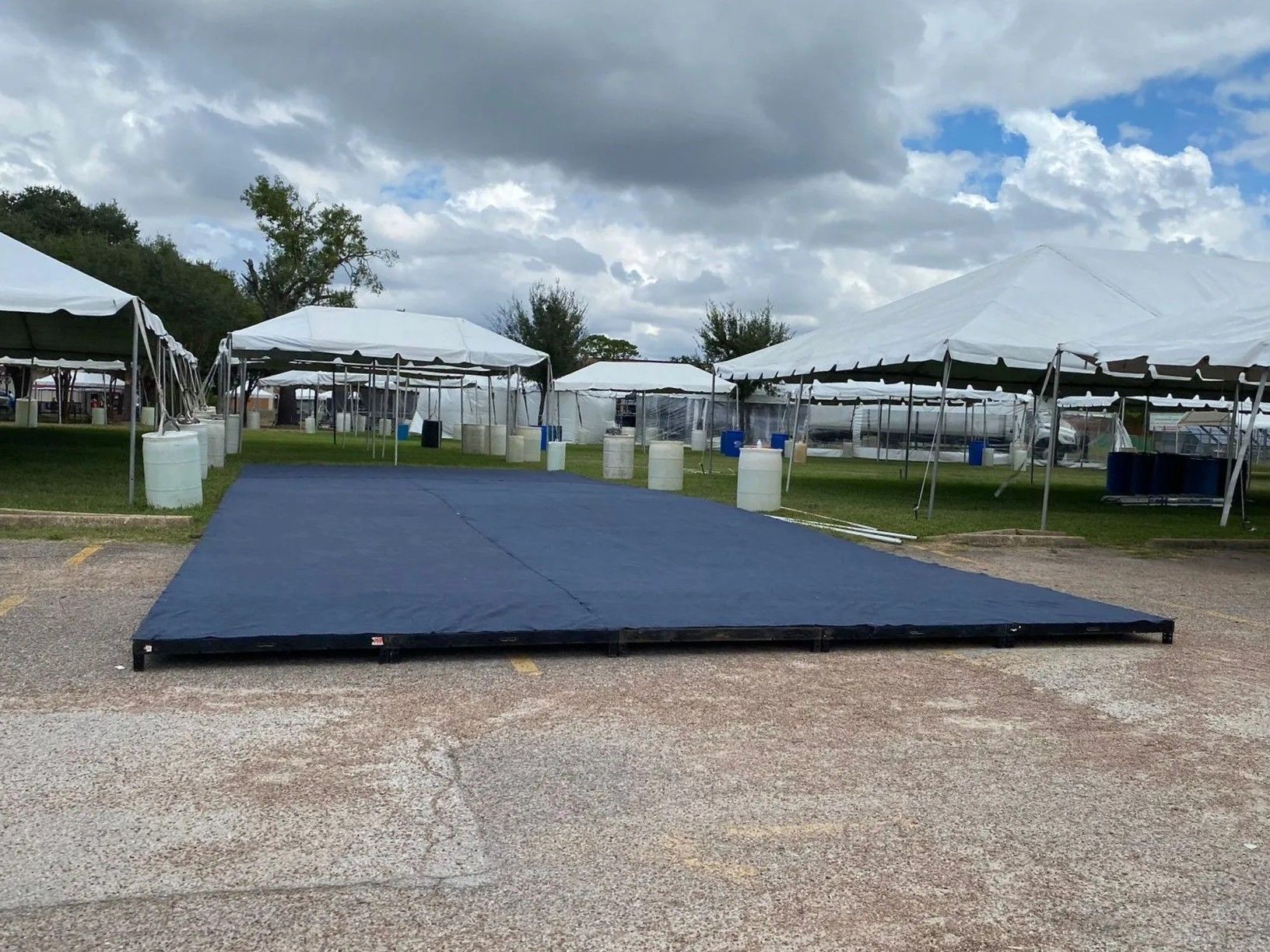 A blue dance floor sits outside with white tents in the background, under a cloudy sky.