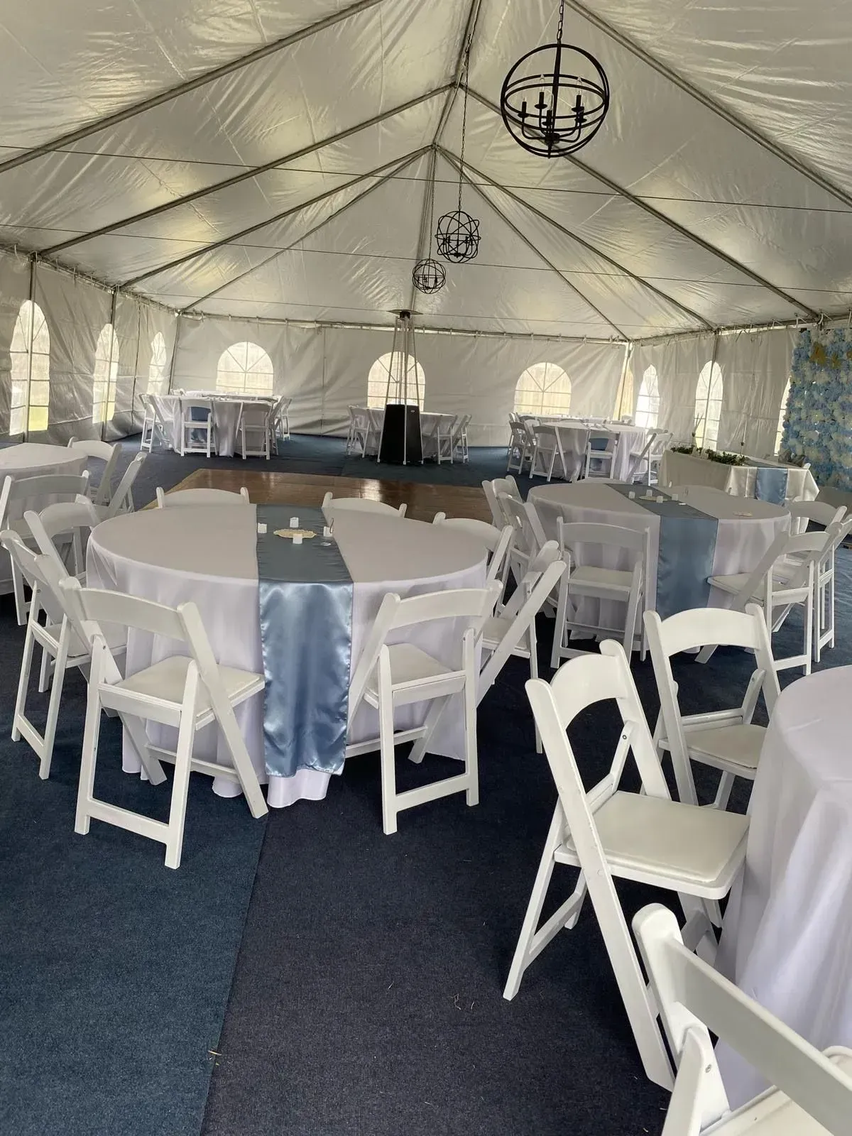 Wedding reception tent with tables, white chairs, and blue accents.