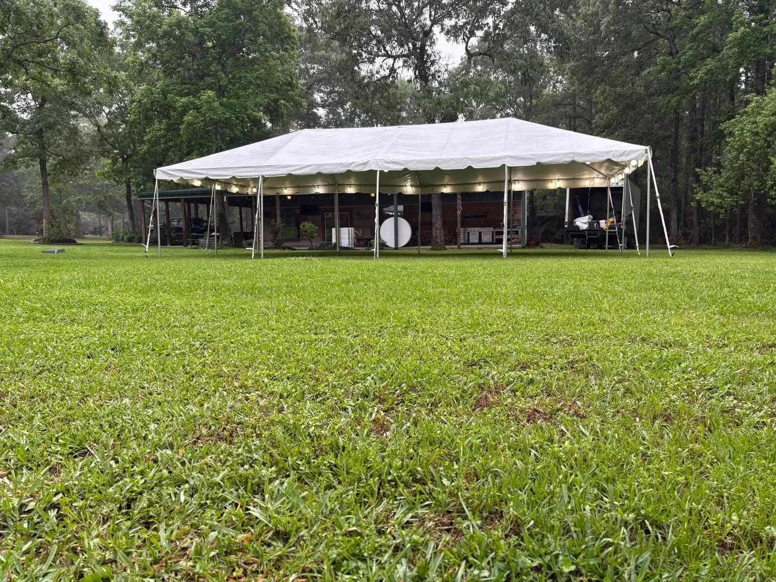 White tent set up on green lawn in a wooded area.