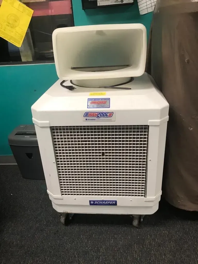 White evaporative cooler with front grill, top air outlet, and wheels.