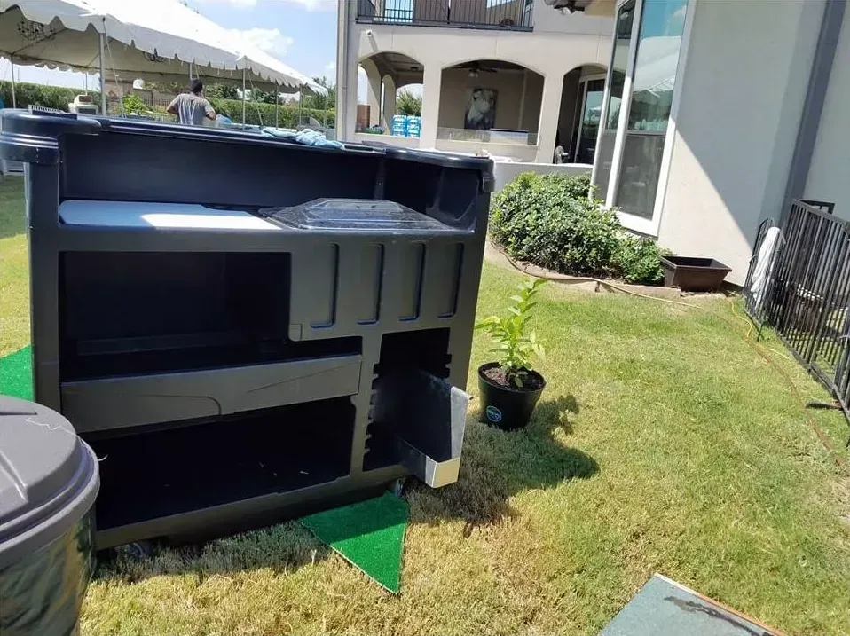 Black outdoor bar on green grass, next to a potted plant and a large house.
