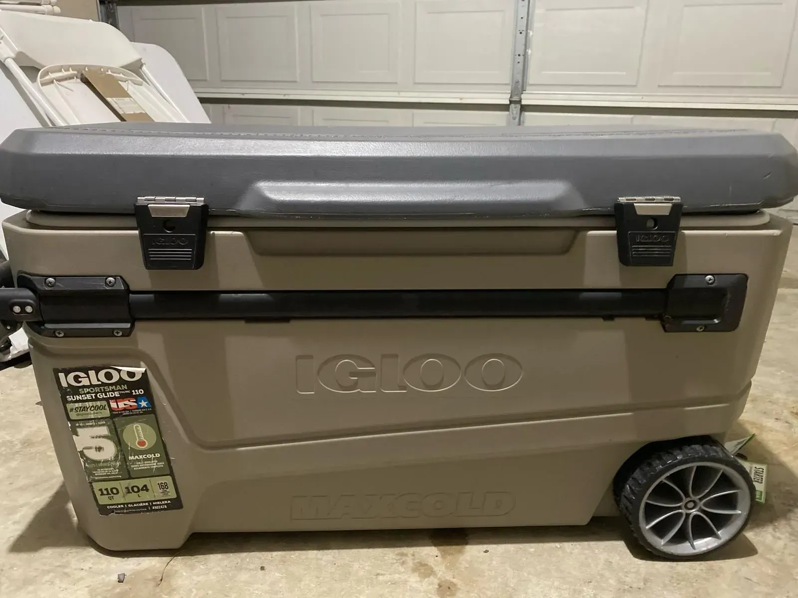 Tan Igloo cooler with gray lid and wheels, indoors.