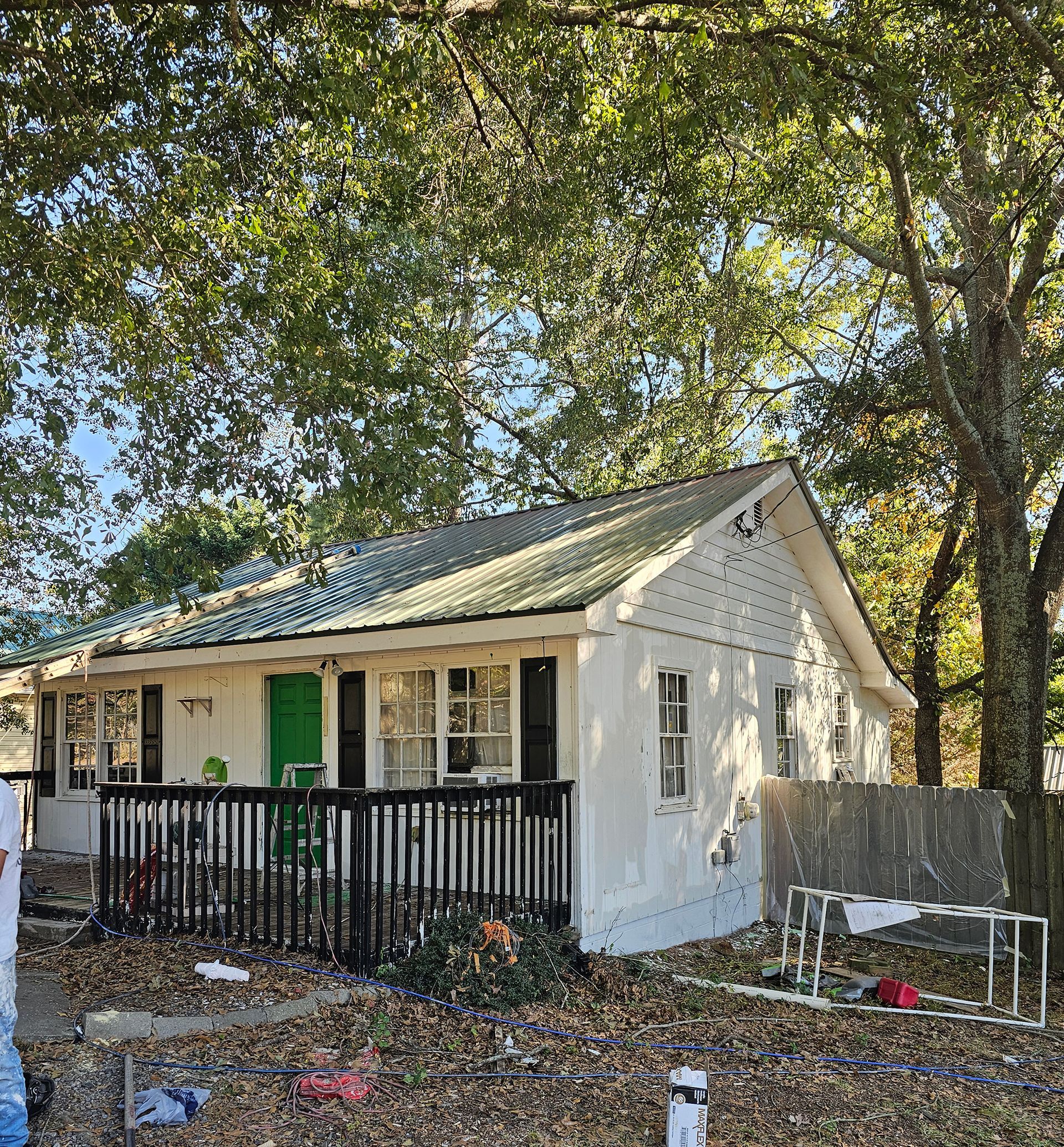 A small white house with a green door is surrounded by trees.