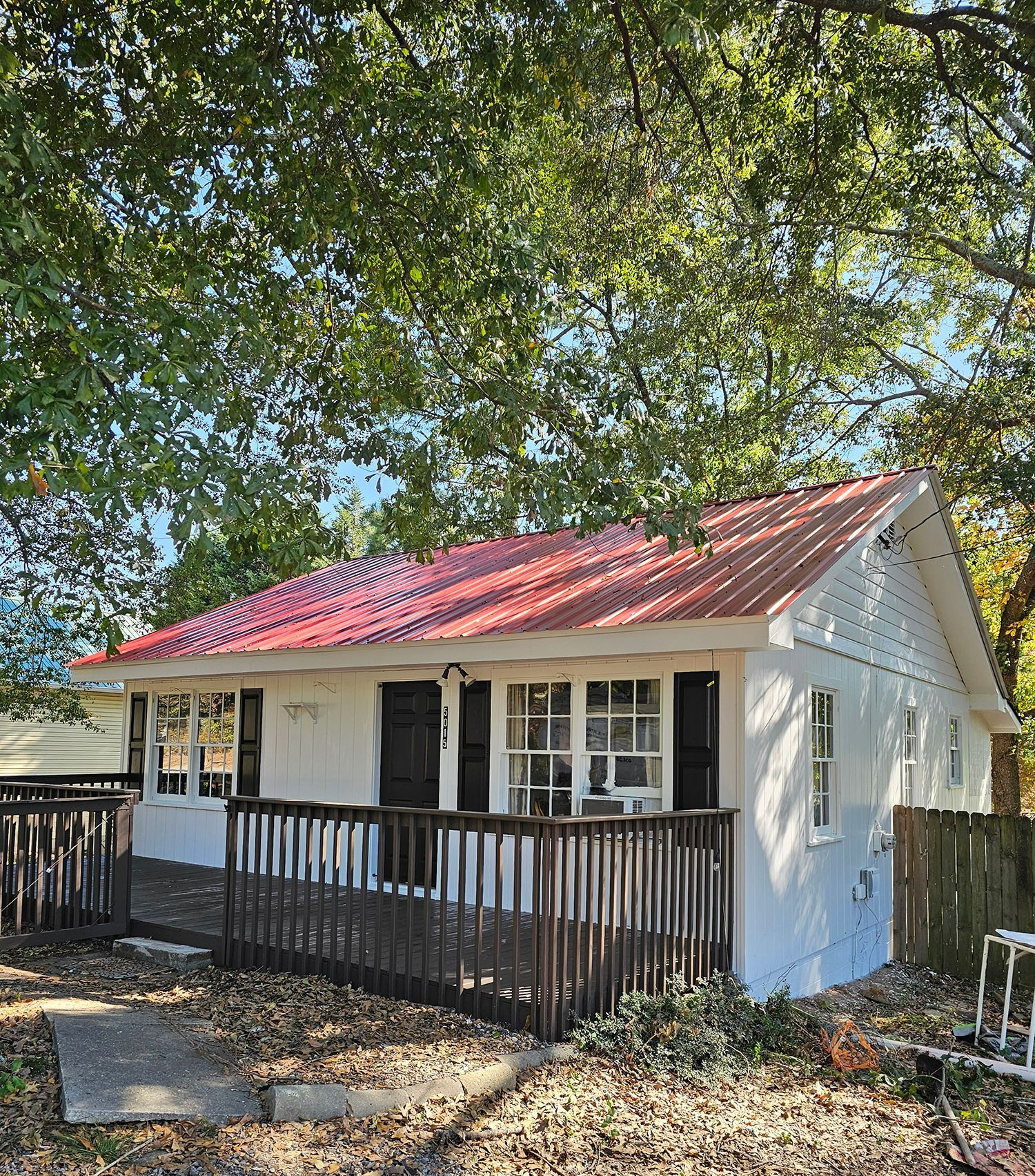 A small white house with a red roof and a deck.