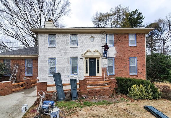 A man is painting a brick house white.