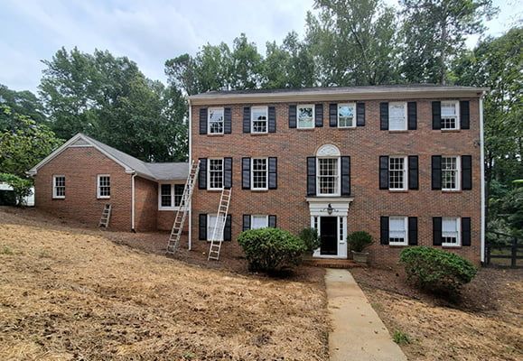 A large brick house with black shutters is sitting on top of a dirt hill.