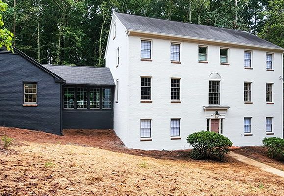 A large white house with a black roof is surrounded by trees.