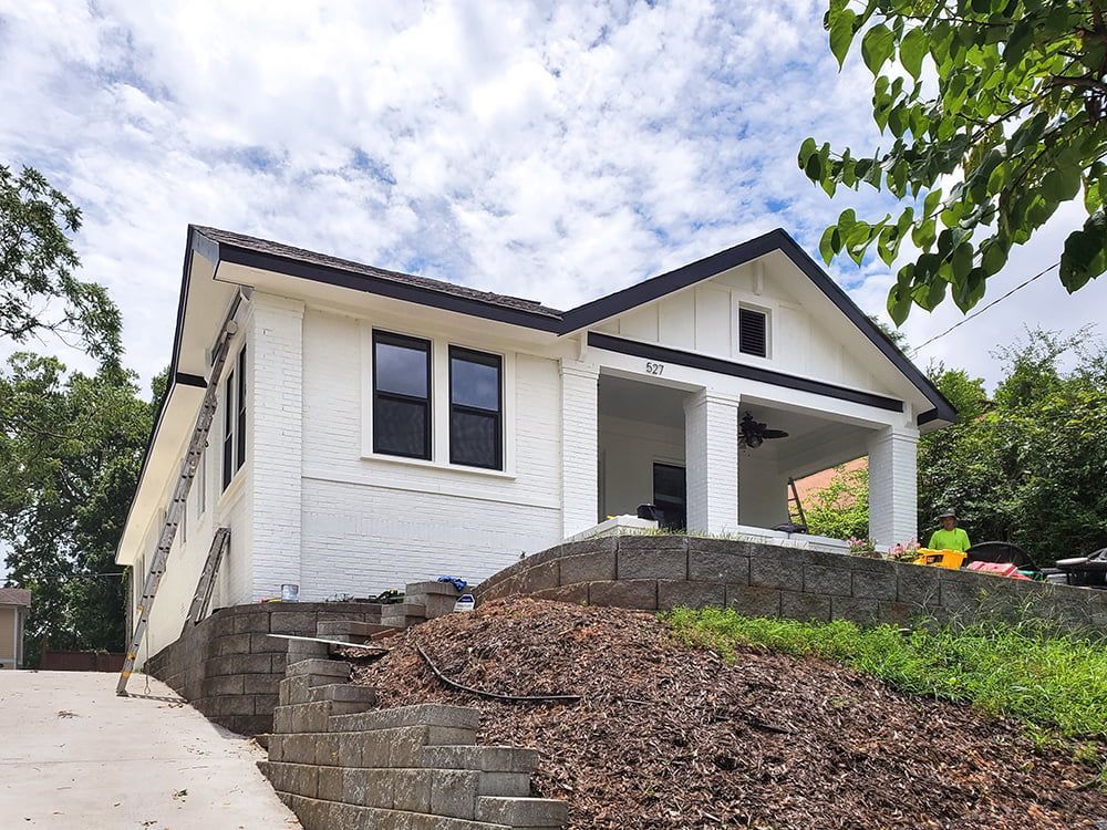 A white house with a black roof is sitting on top of a hill.