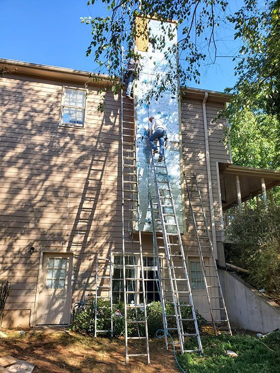 A man is standing on a ladder on the side of a house.