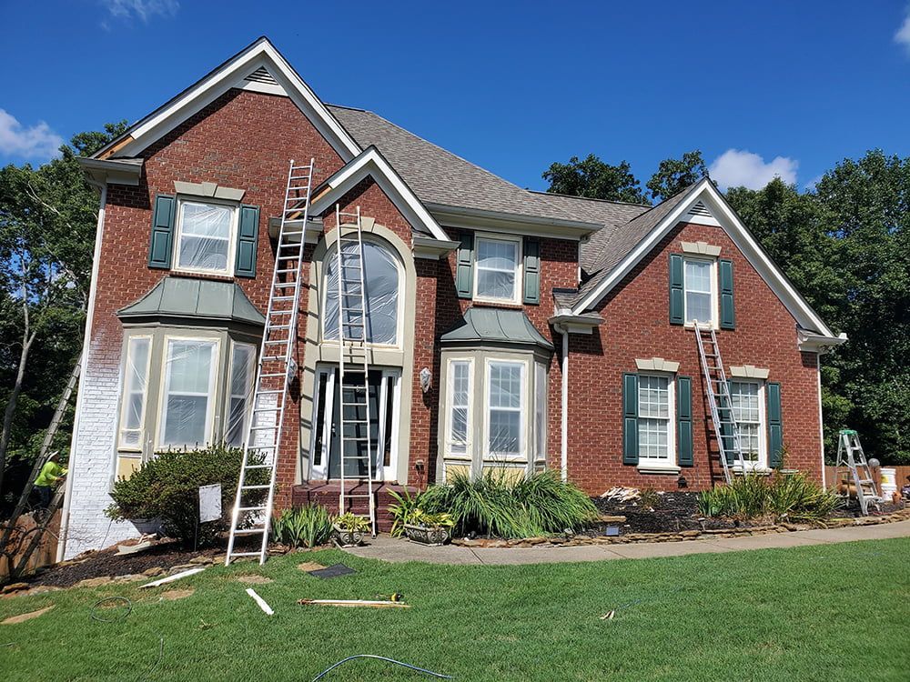 A large brick house with green shutters is being painted.