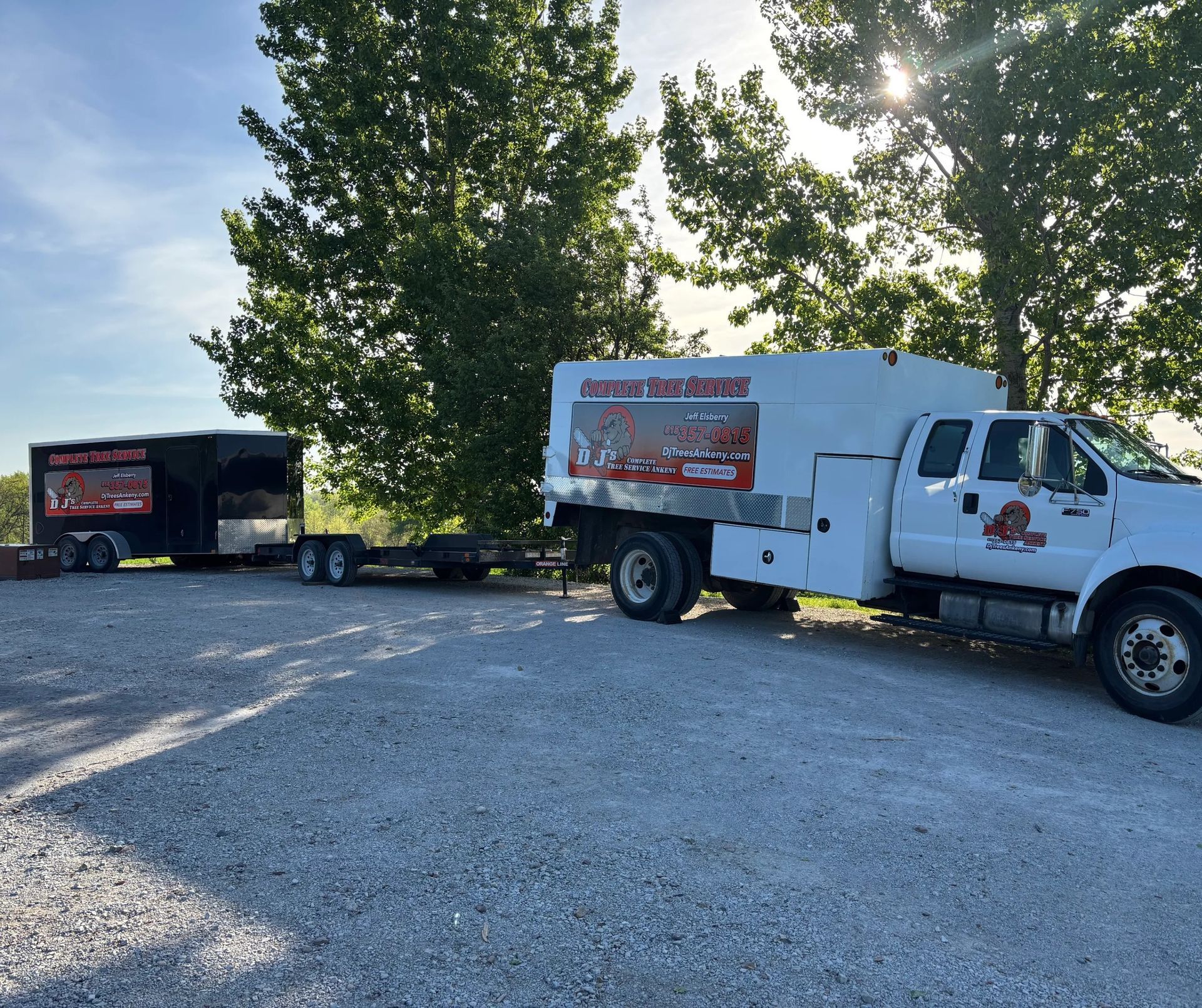 White work truck and black trailer with business logos parked on gravel.