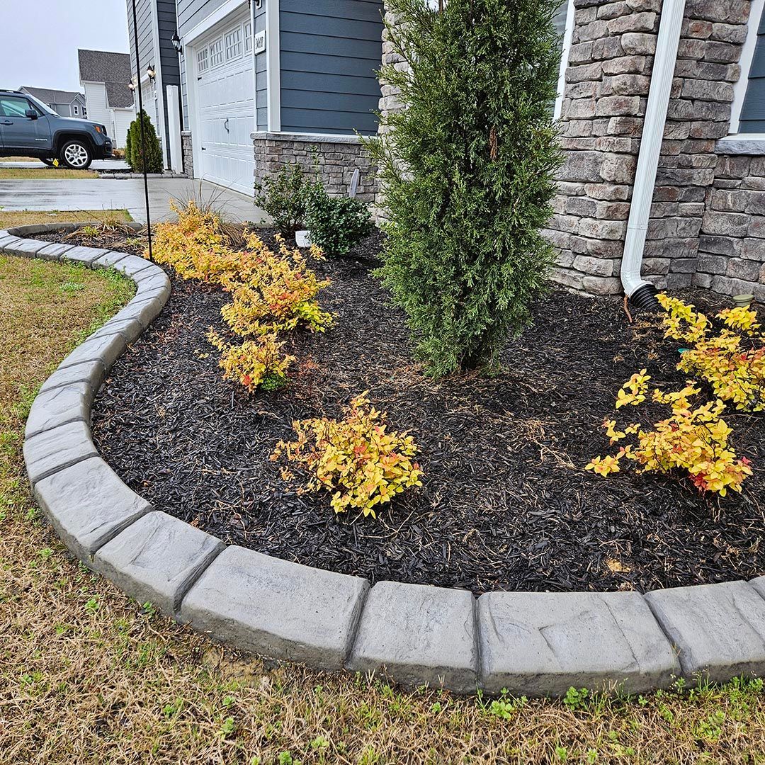 A cobblestone curb surrounds a garden in front of a house.