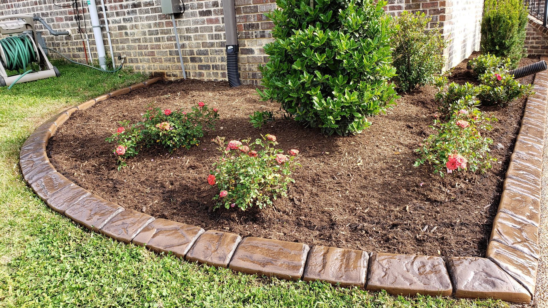 a garden with flowers and mulch in front of a brick house