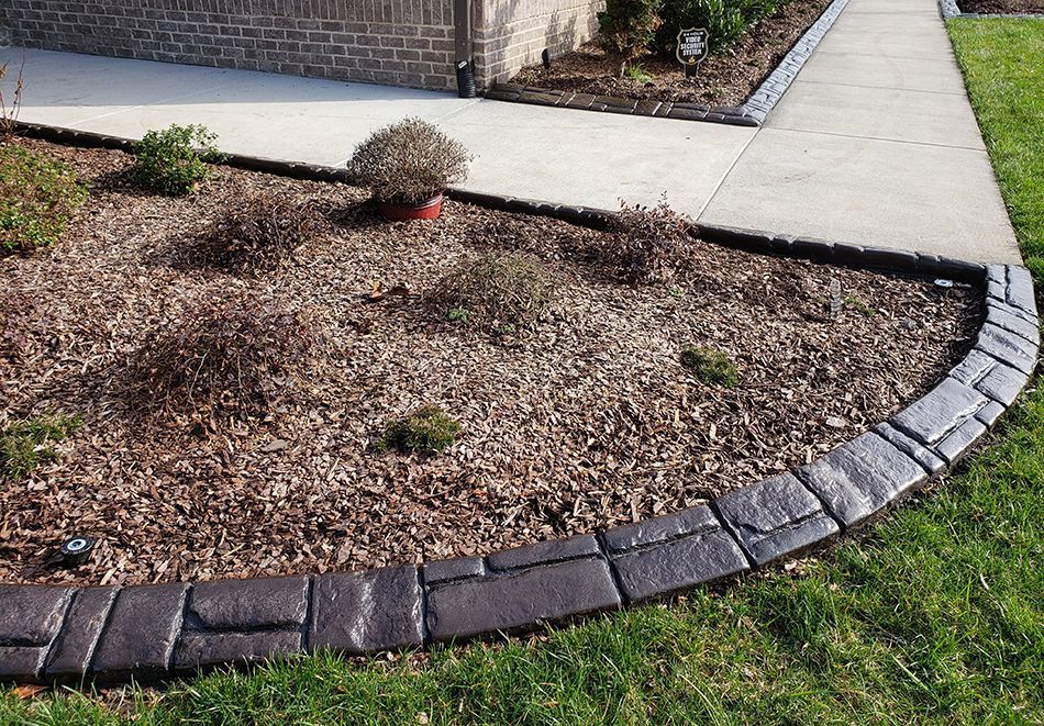 A brick border surrounds a garden next to a sidewalk.