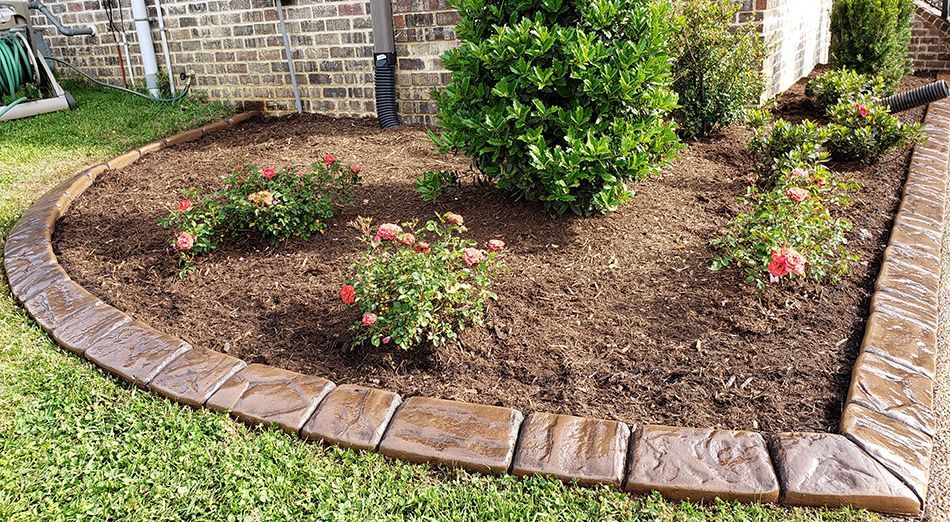 A garden with flowers and a brick border in front of a brick building.