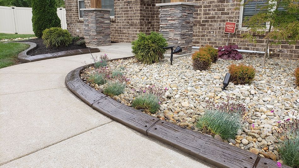 A brick house with a concrete driveway and a rock garden in front of it.