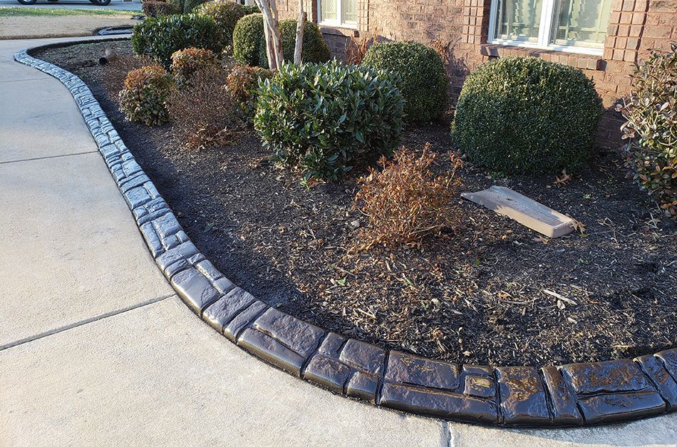 A concrete curb surrounds a garden in front of a brick house.