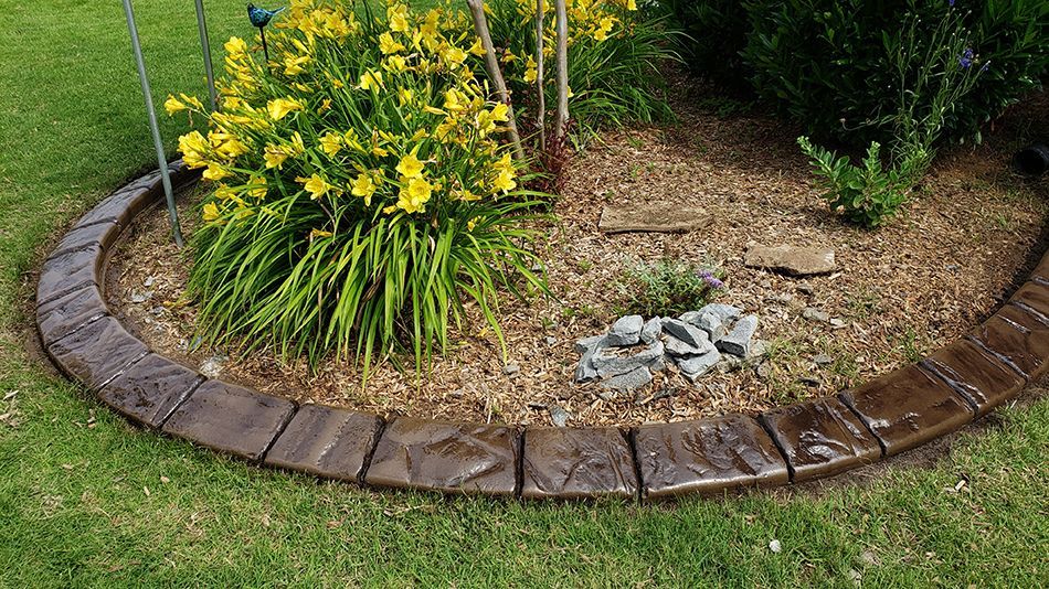 A garden with yellow flowers and a stone border around it.