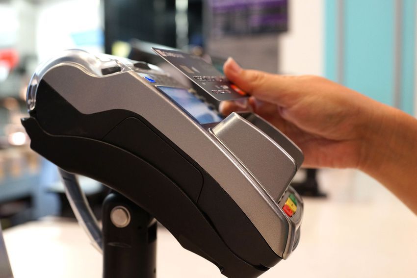 Hand holding credit card near a point-of-sale terminal, ready to pay.