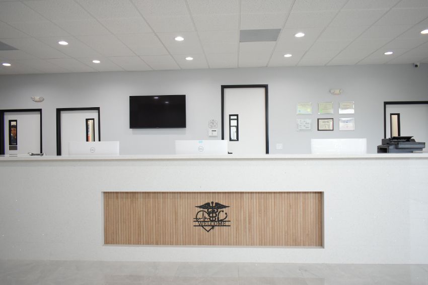Reception desk in a medical office. White counter with a wood-paneled logo in the middle.
