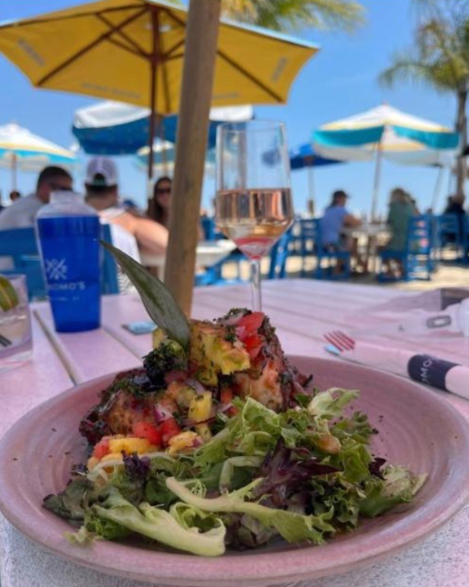 Colorful salad on a pink plate at a beachside table with umbrellas and ocean in the background