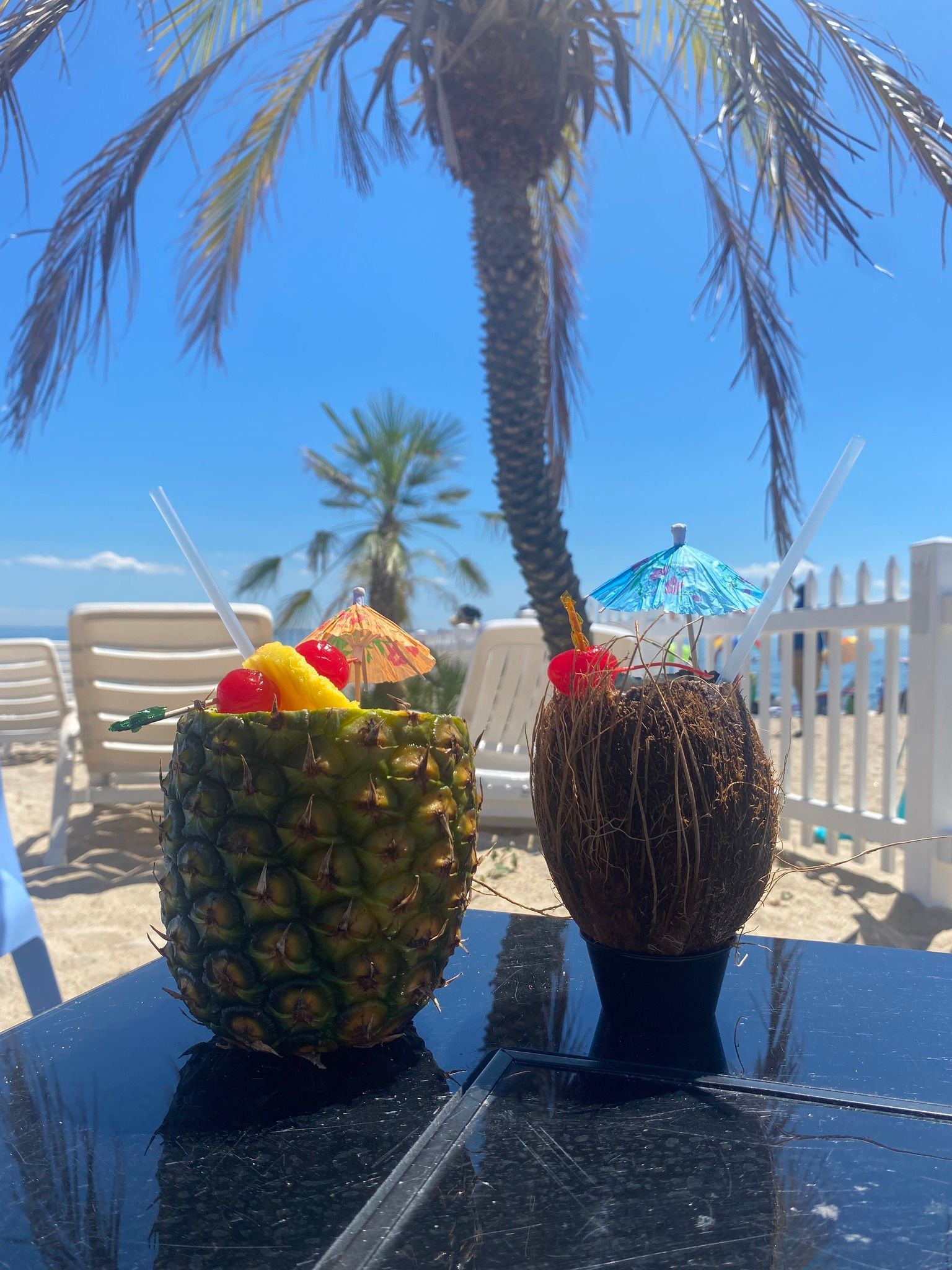Two pineapples filled with fruit are sitting on a table on the beach.