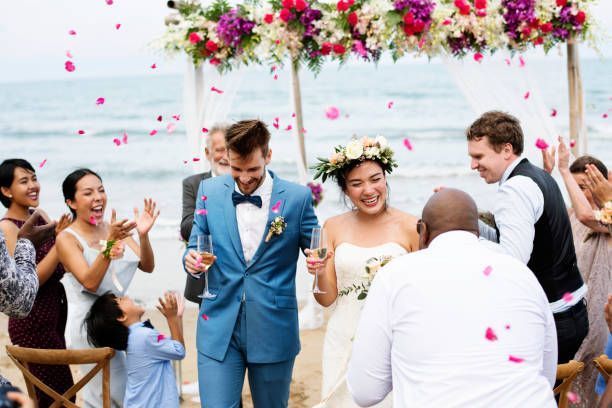 Newly married couple walking down the aisle at a beach wedding, surrounded by cheering guests and flower petals.