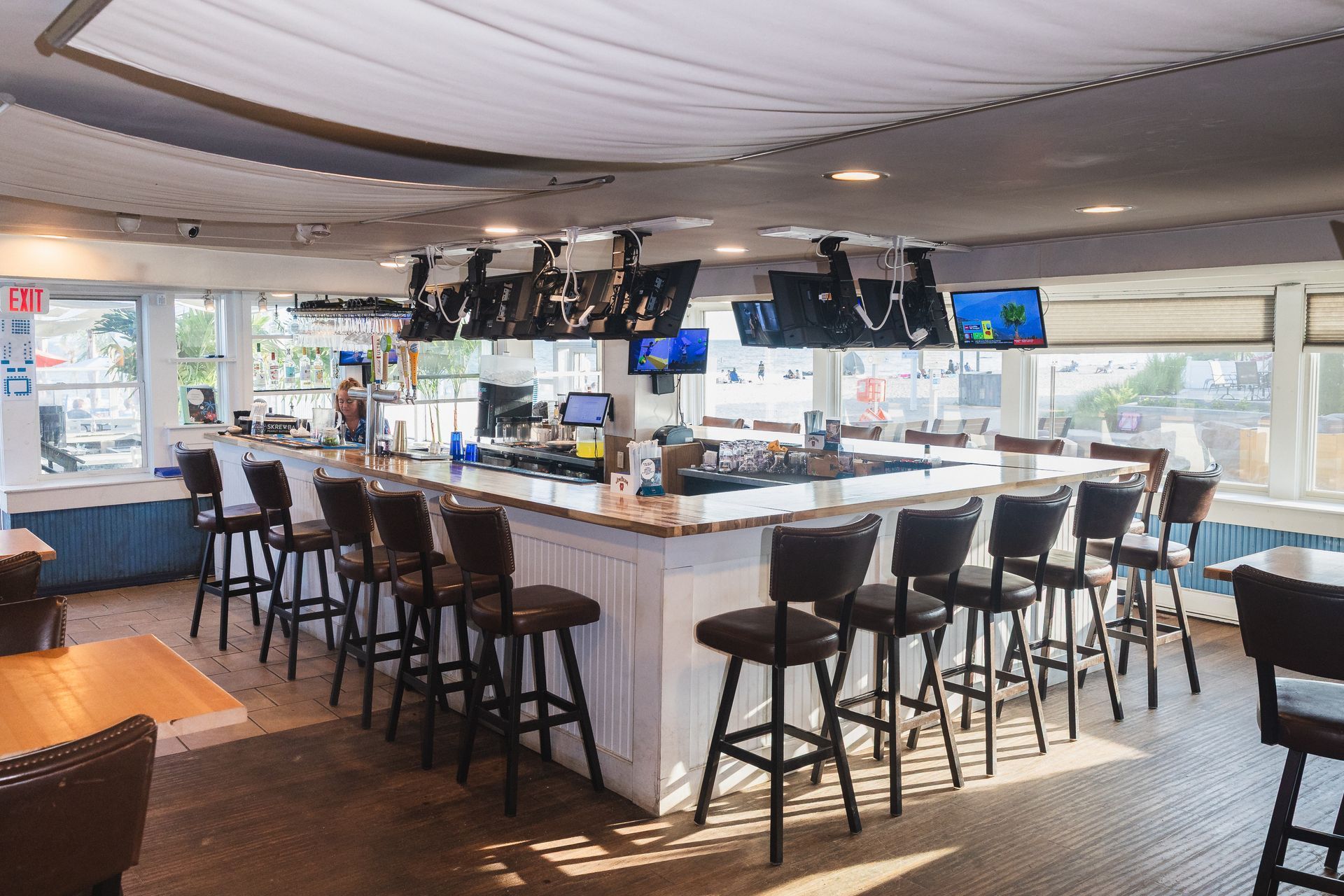 A bar with stools and multiple TVs above it.